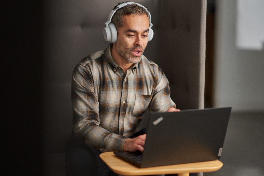 A man watching a webinar while using a cubicle in an open office setting.