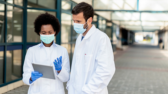Doctors with face masks discussing something on the tablet.
