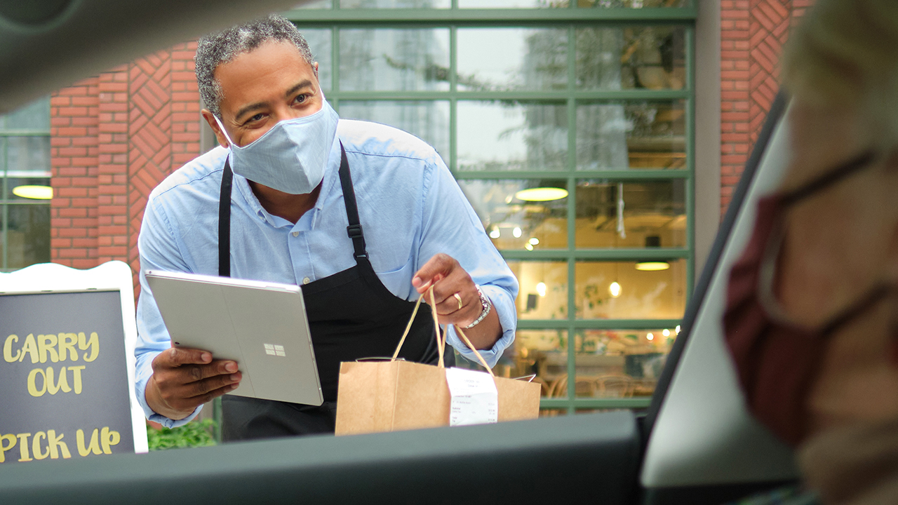 man with a mask delivering food to driver in the car.
