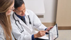 Doctor pointing out graph on a digital tablet to a patient sitting next to them