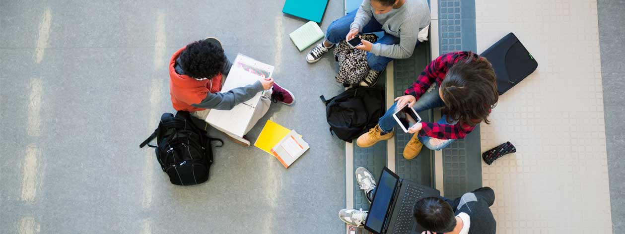 An aerial view of a group of students studying with laptops, tablets, and smartphones