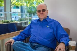 Apple sits at a chair in an open space in a Microsoft building.